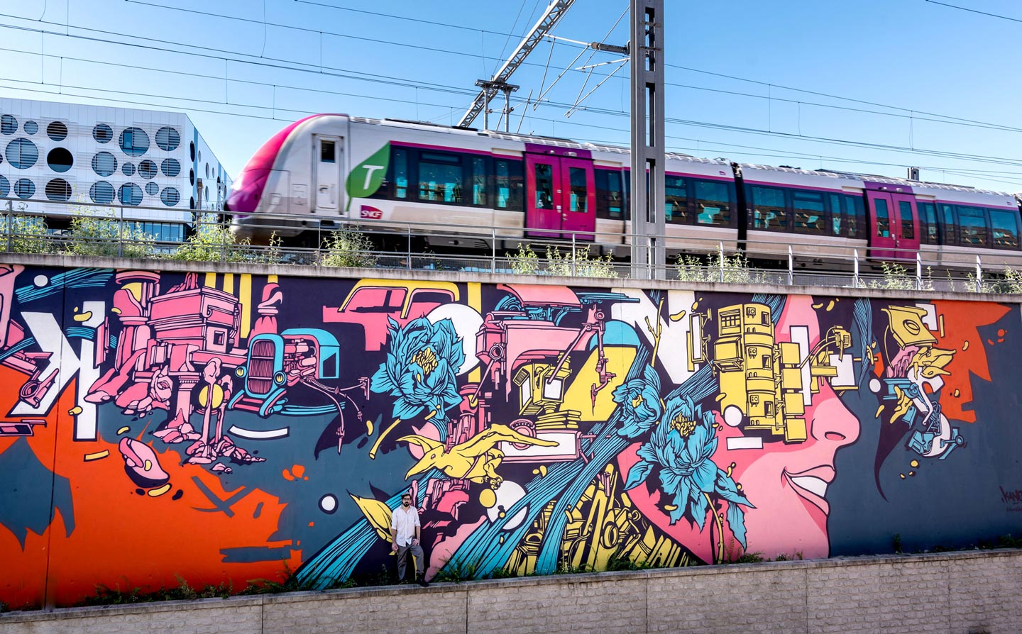 alex kanos stand on with a graffiti wall painted in background and above there is a railroad with a train